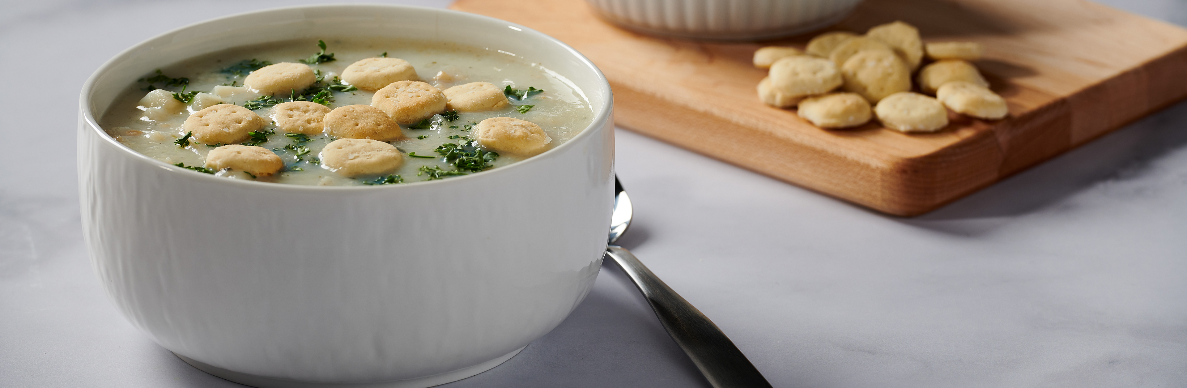 Bowl of soup with beans and greens on a table with a cutting board in the background