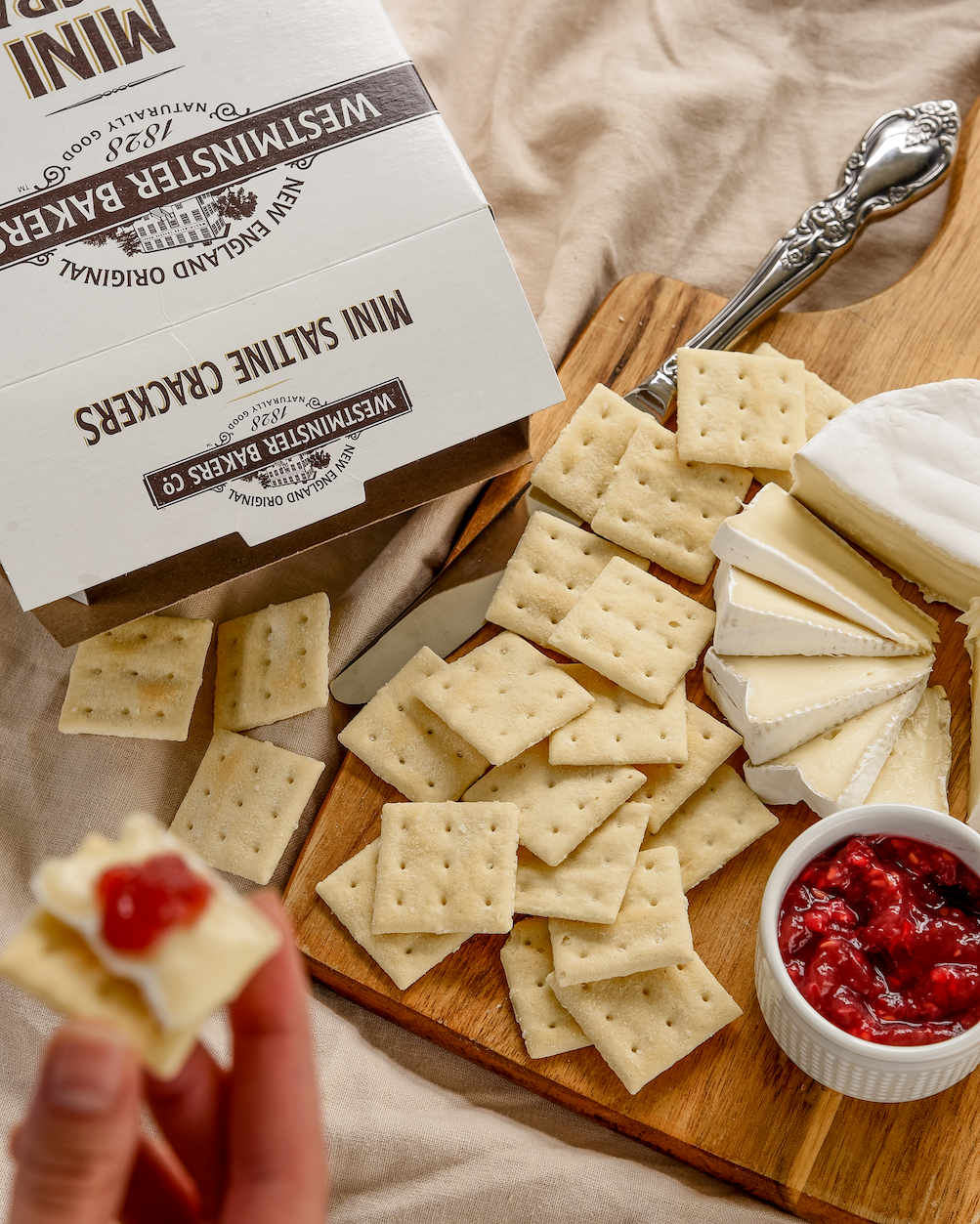 Wooden board with crackers, cheese, and red sauce next to a box of Westminster Bakers crackers.