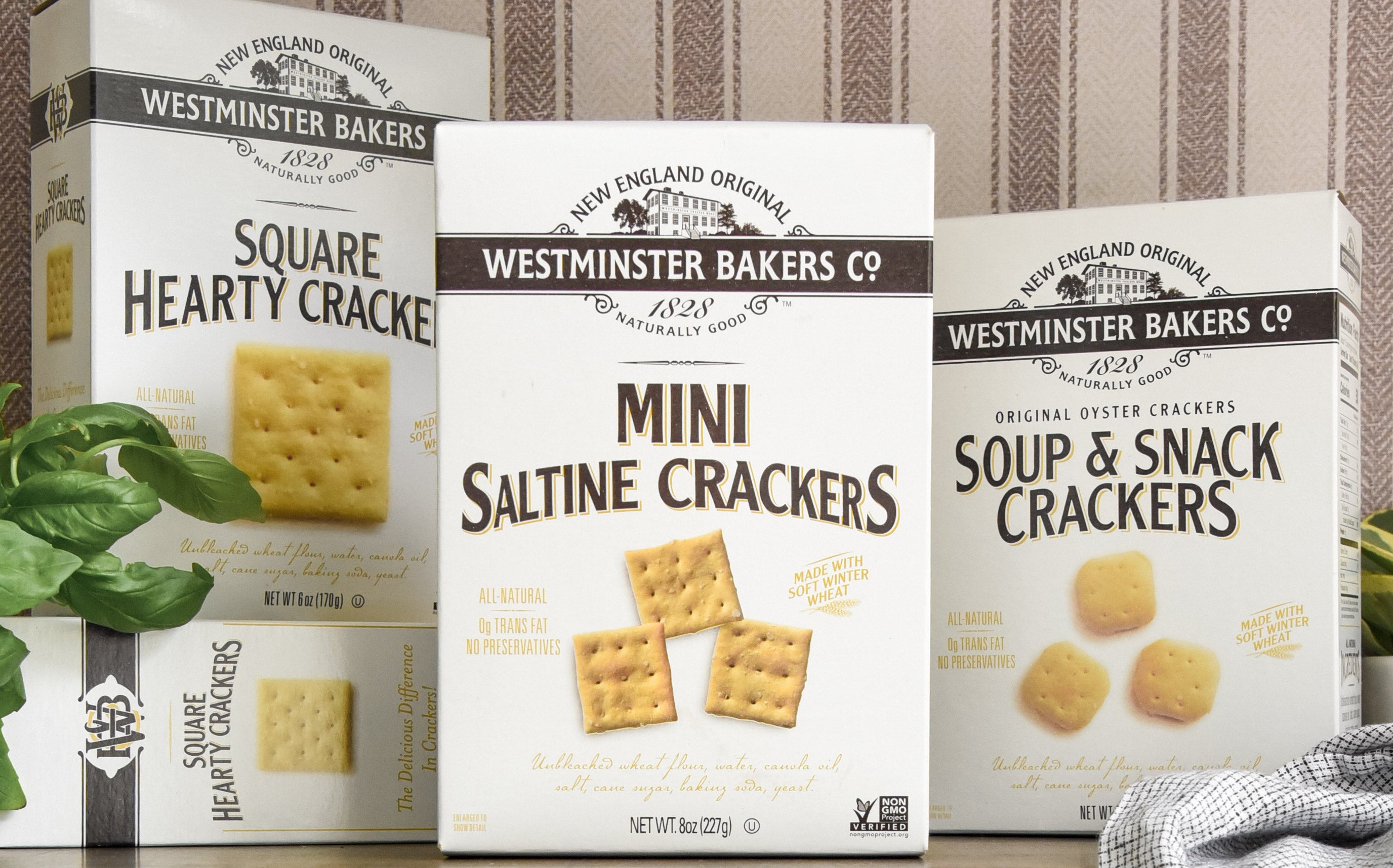 Three boxes of Westminster Bakers crackers on a wooden surface with a striped wall background.