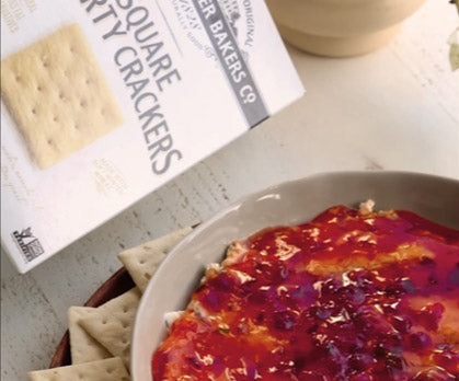 Dip with crackers on a table next to a box of crackers